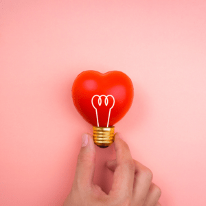 Hand holding a heart shaped red light bulb