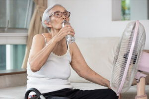 older woman drinking a bottle of water in front of a fan