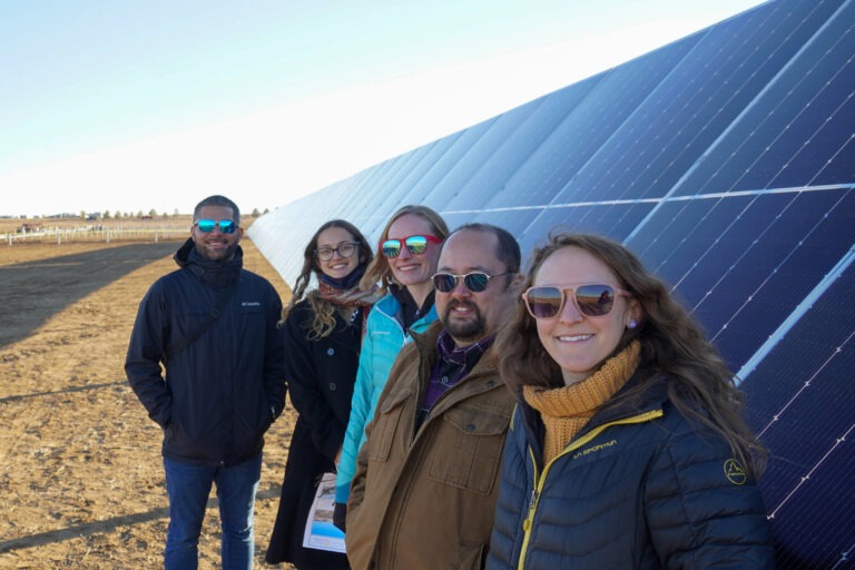 EOC solar team stands alongside solar panels in a field